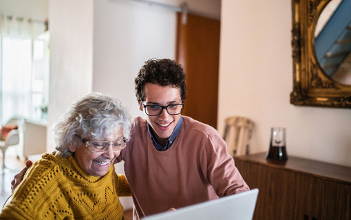 Jeune homme aux côté d'une dame âgée, les deux regardant un ordinateur et riants